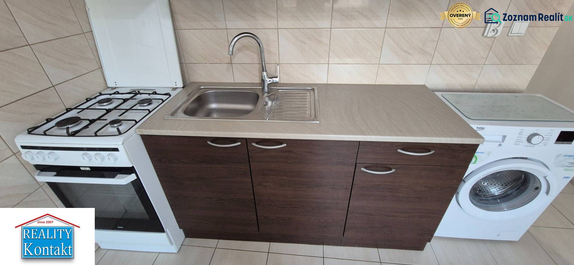 Kitchen in a studio apartment with a stove, sink, and washing machine, light tiled wall.
