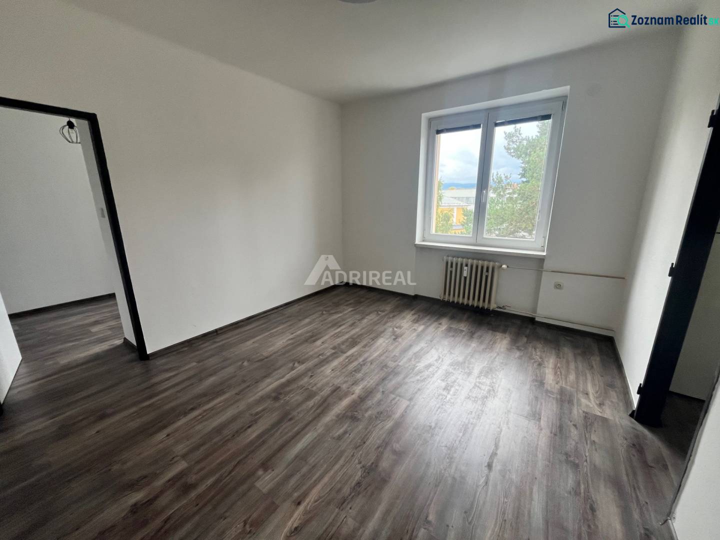 A room in a 3-room apartment with a wood-patterned floor and a large window.