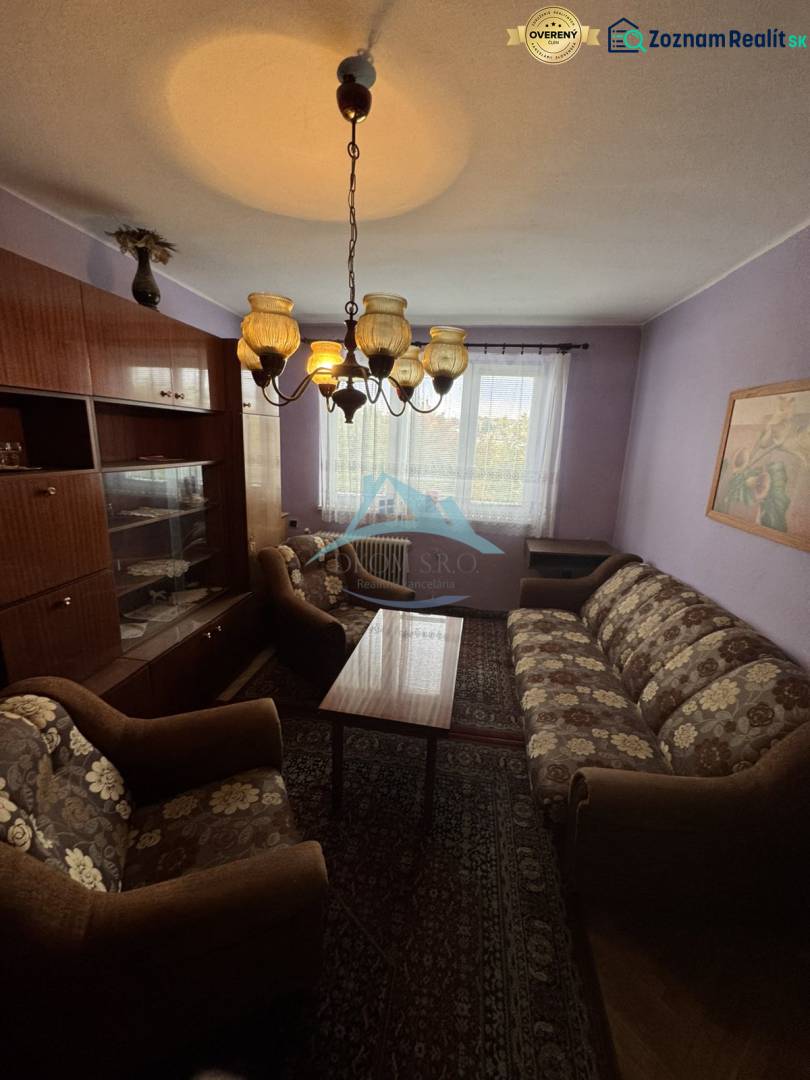 Living room in a two-room apartment with older furniture, a sofa, and a chandelier.