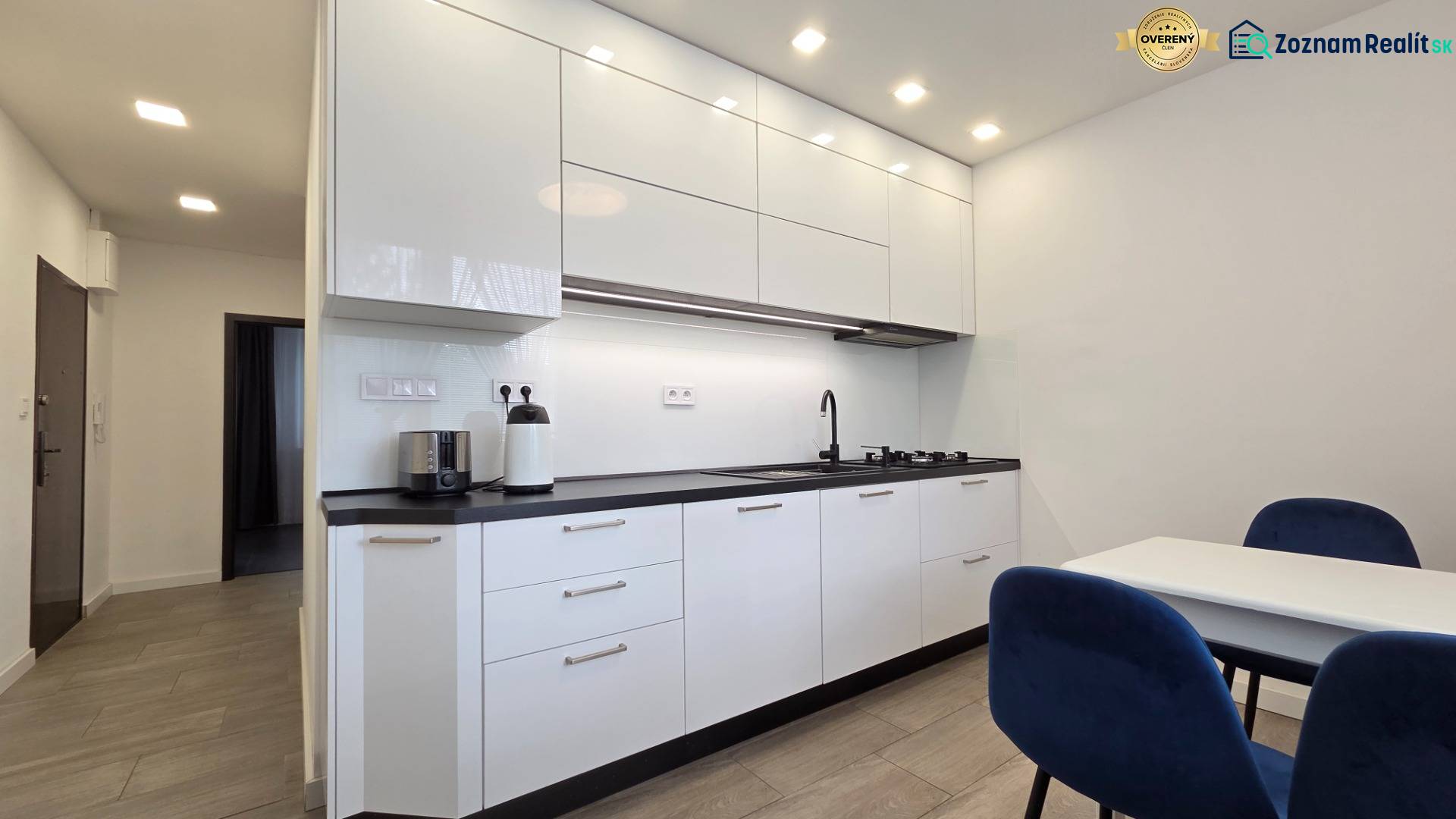 A kitchen in a 3-room apartment with white cabinets and a dining table with blue chairs.