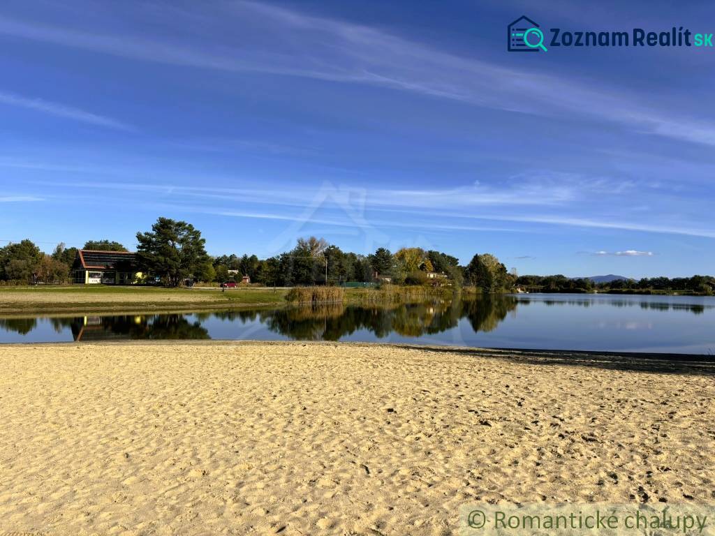 The beach by the cottage in Malé Leváre, surrounded by a lake and greenery on a sunny day.