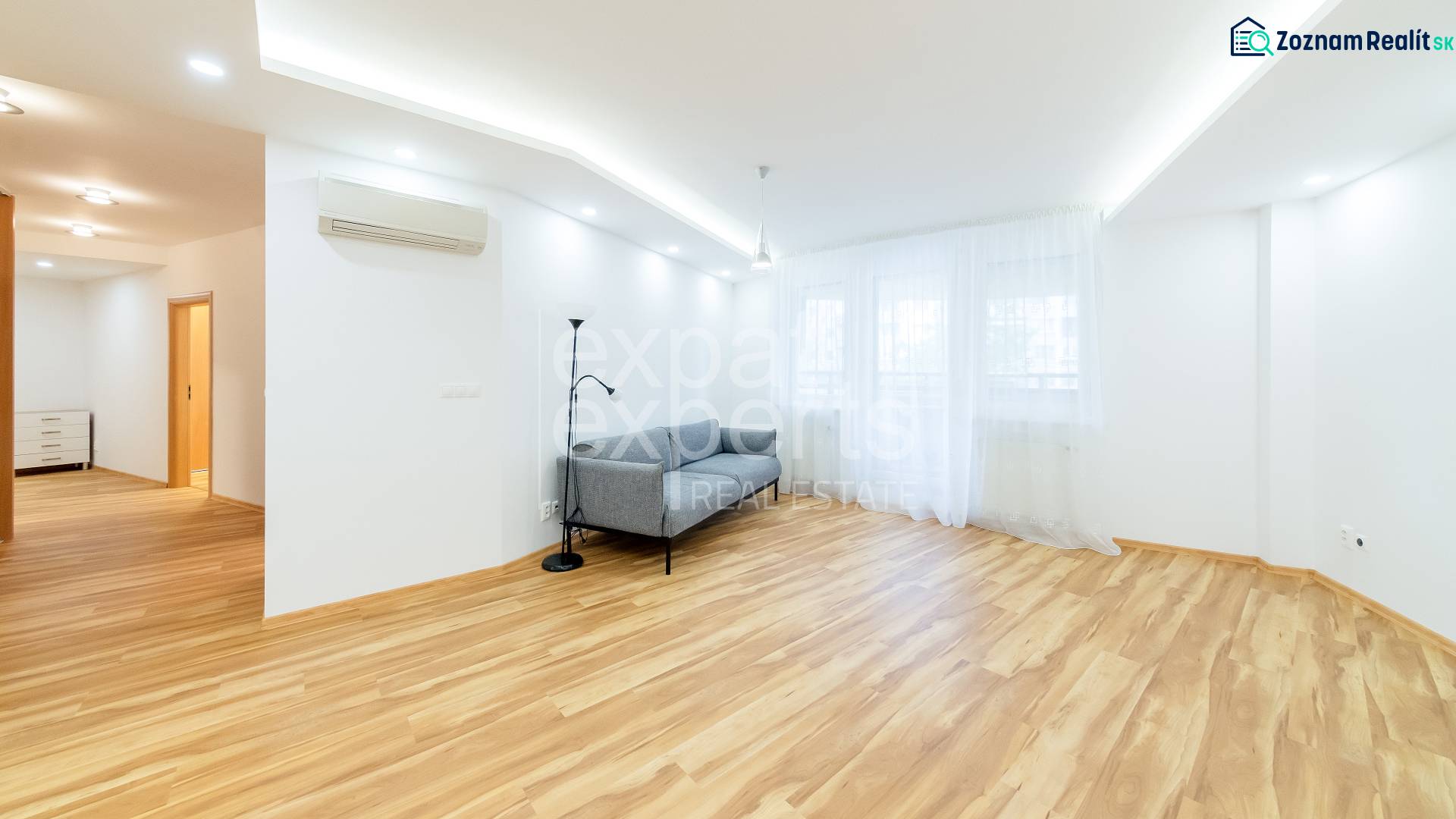 Living room in a three-room apartment with a sofa, white walls, and a wooden decor floor.