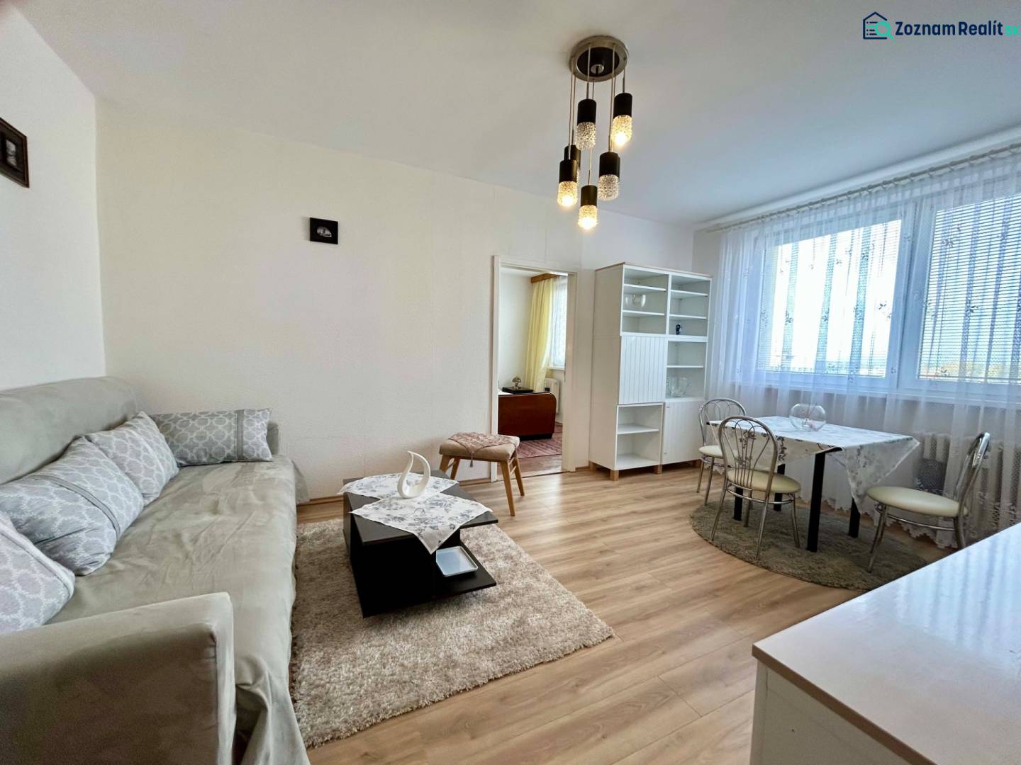 Living room in a two-room apartment with a wooden decor floor and a gray sofa.