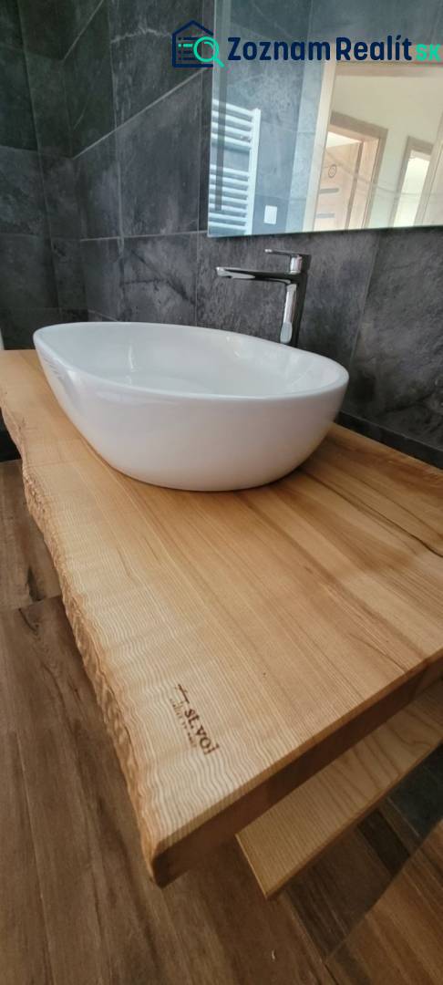 A bathroom in a family house with a sink on a wooden countertop and dark tiles.