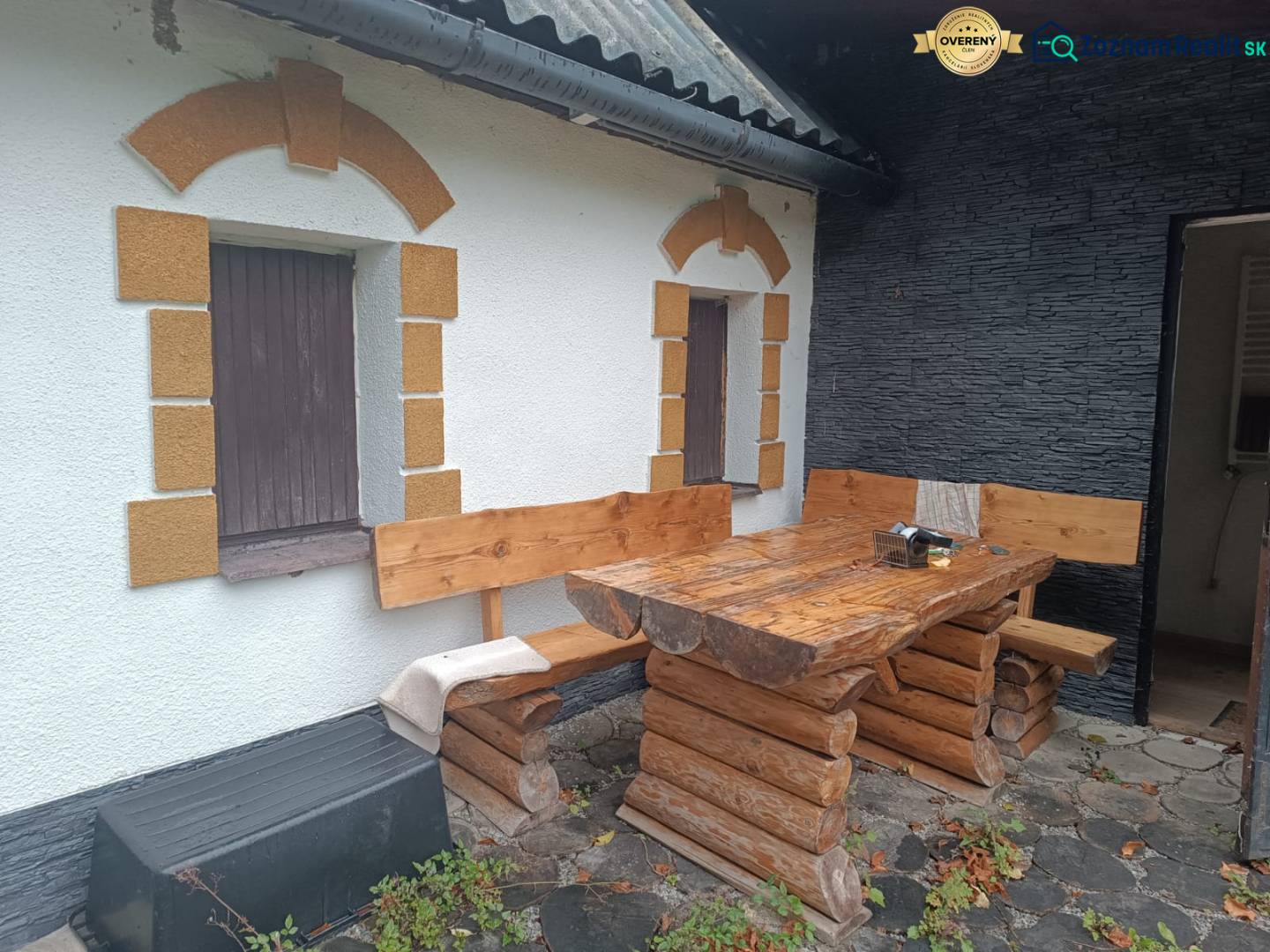 A cottage in Píla with wooden seating on a stone terrace and decorated windows.