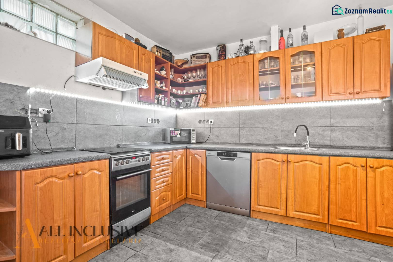 A kitchen in a family house with wooden decor, appliances, and gray tiles.