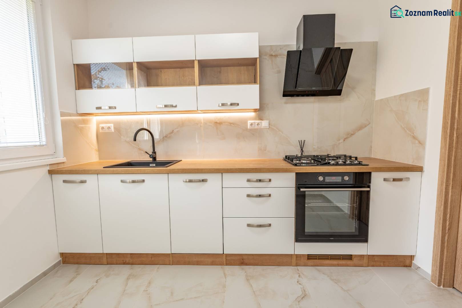 A kitchen with white cabinets, a black range hood, a cooktop, and a floor with a wood design.