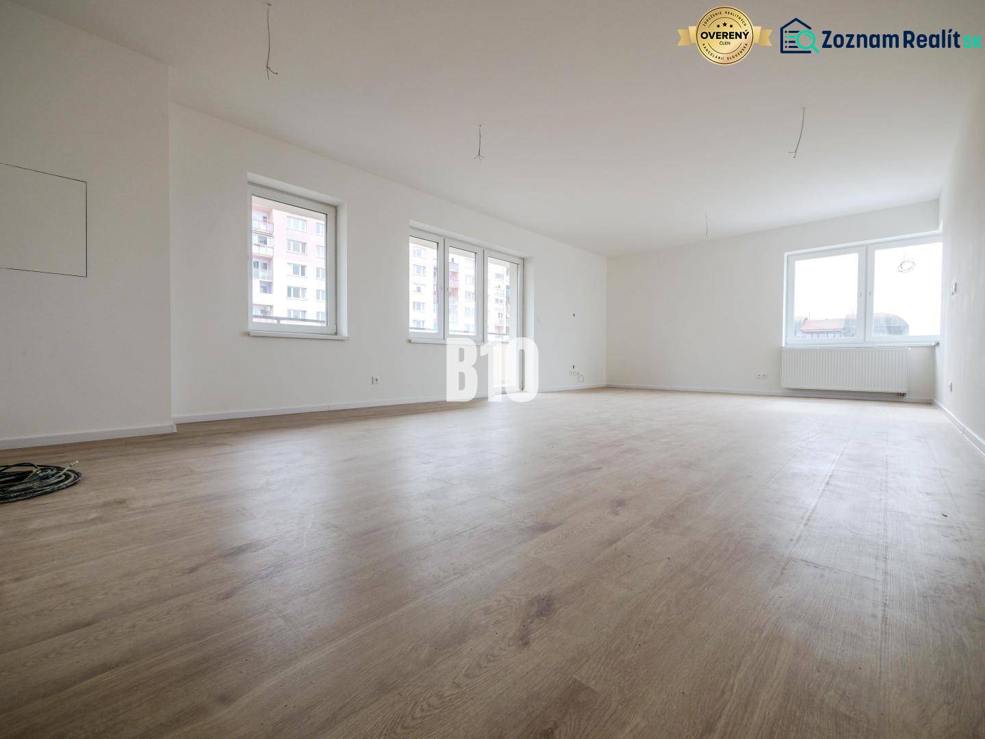 Spacious 3-room apartment with windows, wooden floor, and white walls.