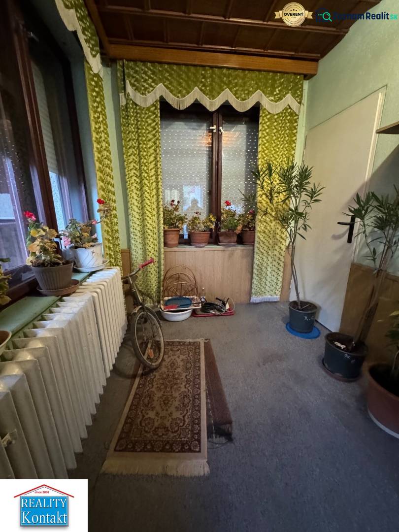 Interior of a family house with flowers, a bicycle, green curtains, and carpets.