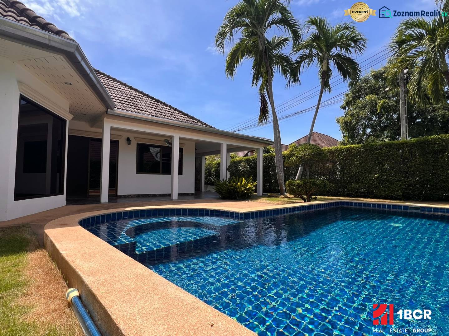 A villa in Pattaya with a garden and a pool, surrounded by palm trees and a hedge.