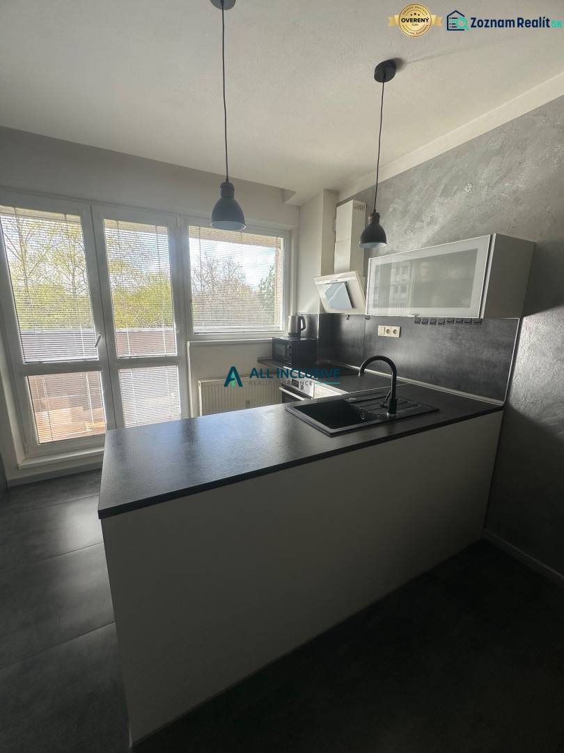 A kitchen in a studio apartment with gray walls, windows, and kitchen cabinets.