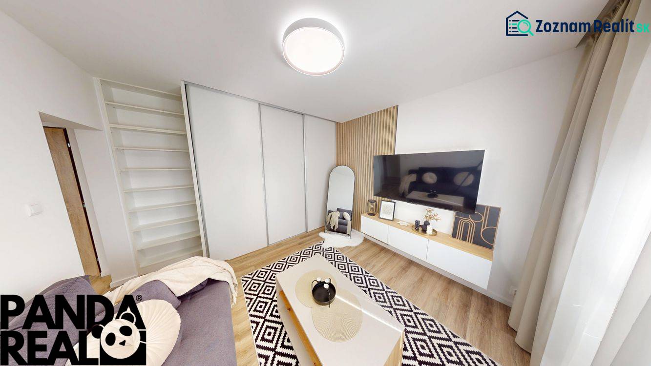 Living room in a studio apartment with a TV, mirror, and wooden decor flooring.