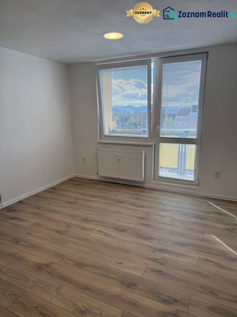 A studio apartment with a wood-patterned floor and a large window offering a view of the surroundings.