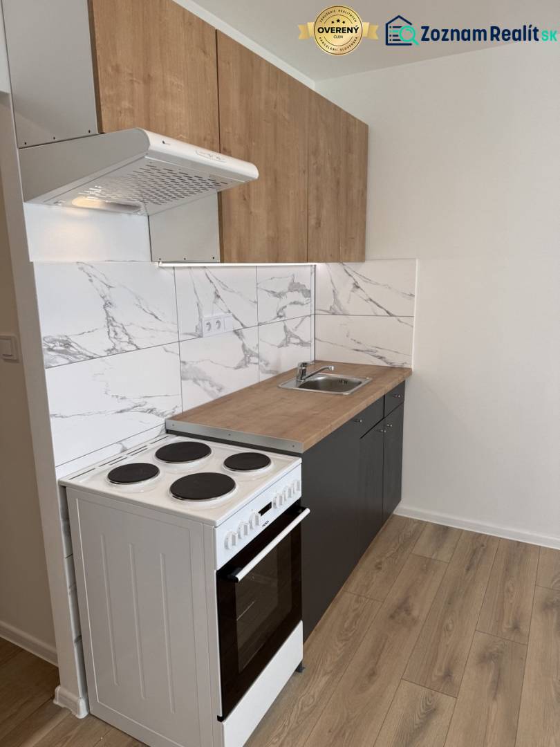 A kitchenette in a studio apartment with an electric stove and a floor with a wooden decor.