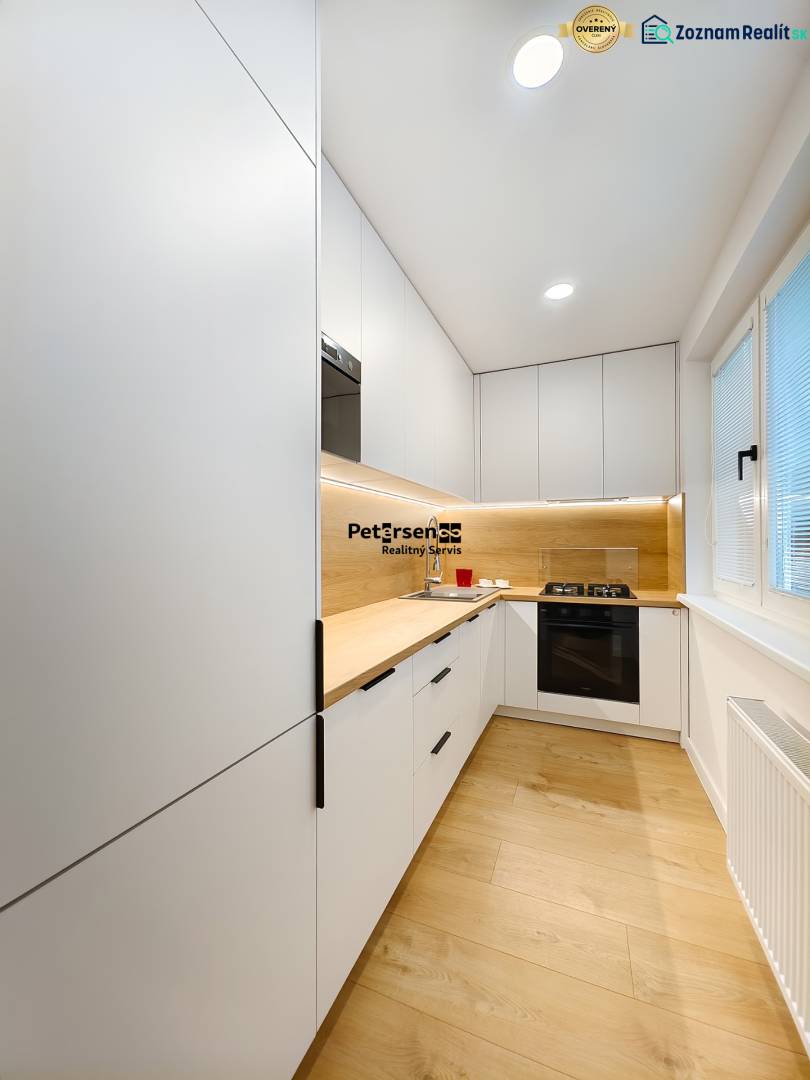 A kitchen in a 2-room apartment with a white kitchen unit and a floor with a wood decor.