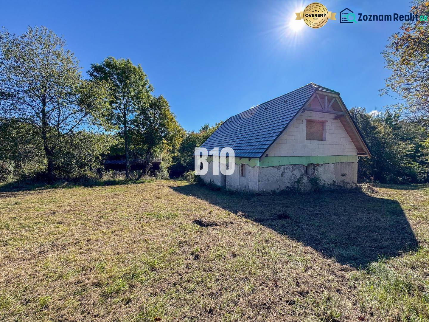 A cottage in Lackov on a sunny meadow surrounded by trees and a blue sky.