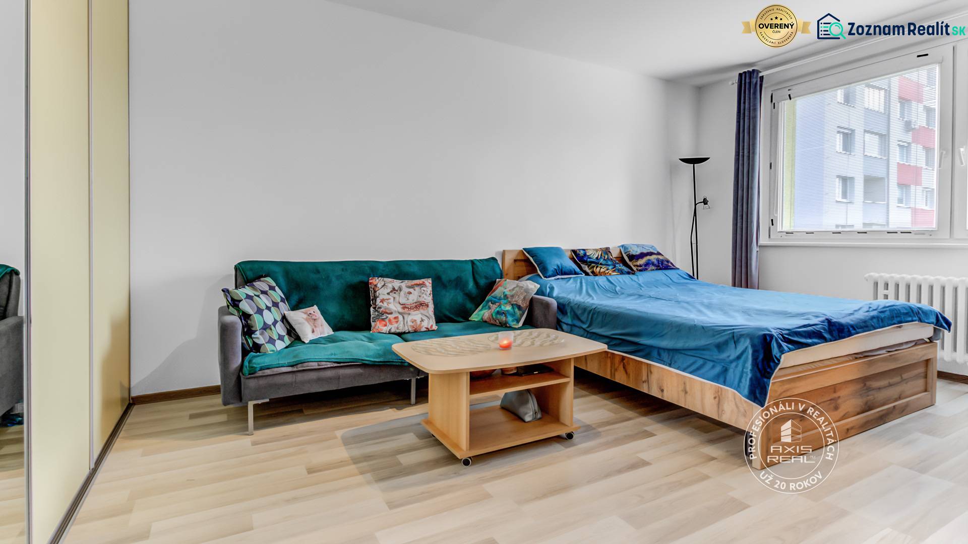 A studio apartment with a sofa, bed, and a table on a floor with a wooden decor.