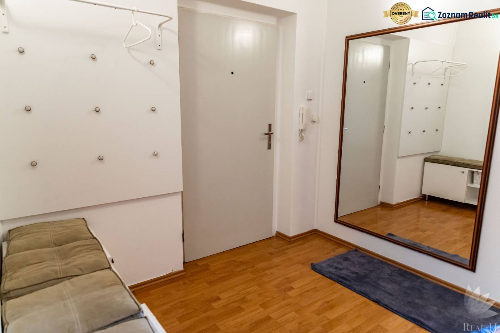 The entrance hall of a 2-room apartment with a wooden decor floor, a mirror, and a coat rack.