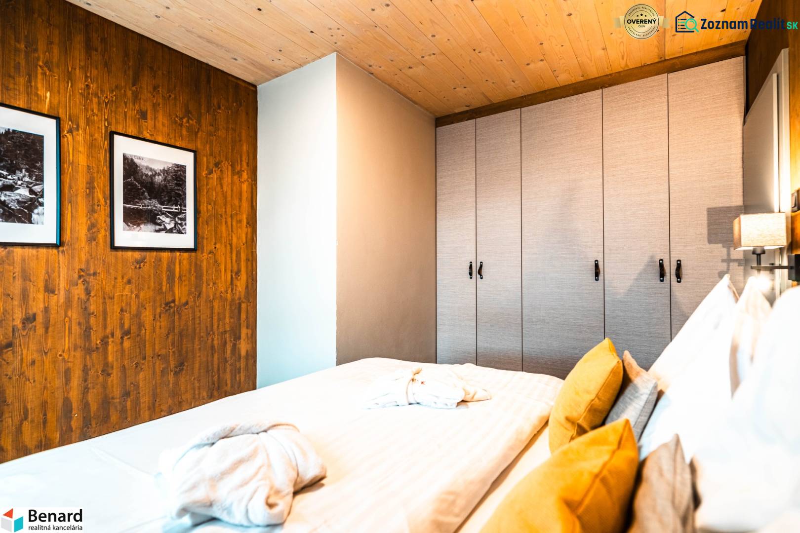 Bedroom in a 2-room apartment with a bed, wardrobe, and pictures on wooden paneling.