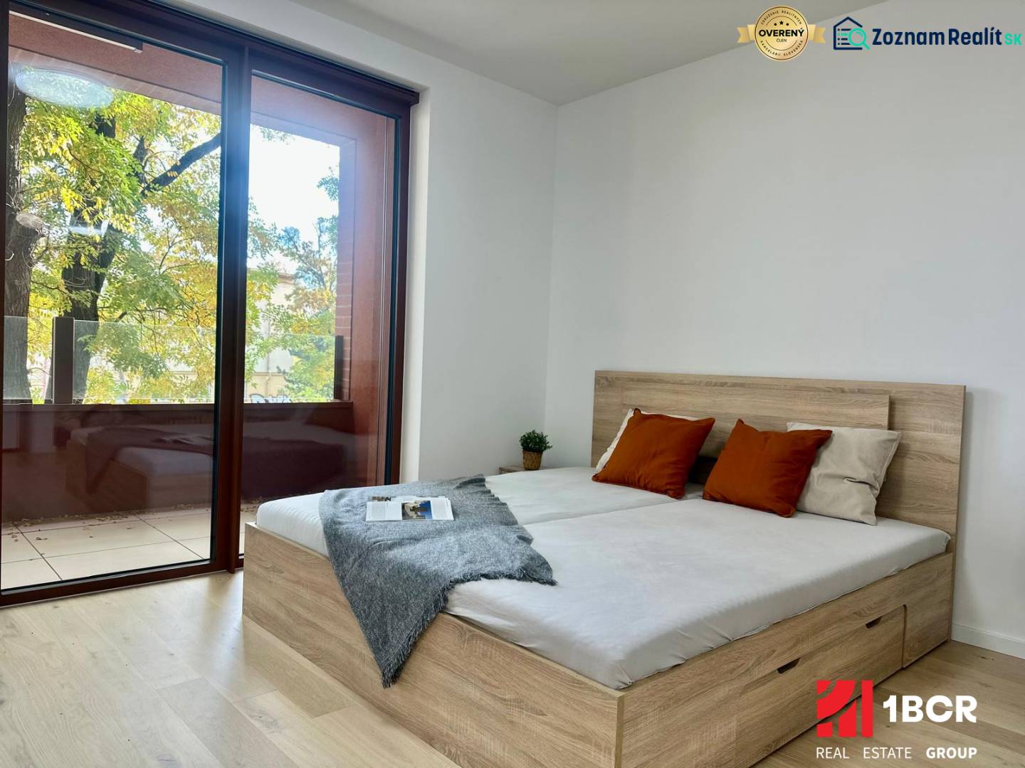 A bedroom with a large window, a bed, and a wooden decor floor in a studio apartment.