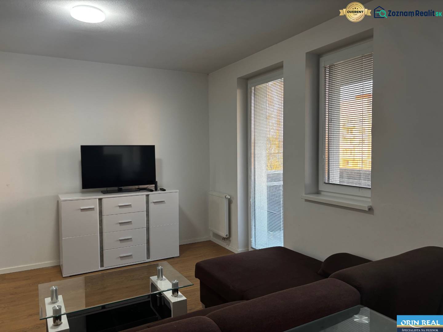 Living room in a two-room apartment with a sofa, television, and wooden decor flooring.