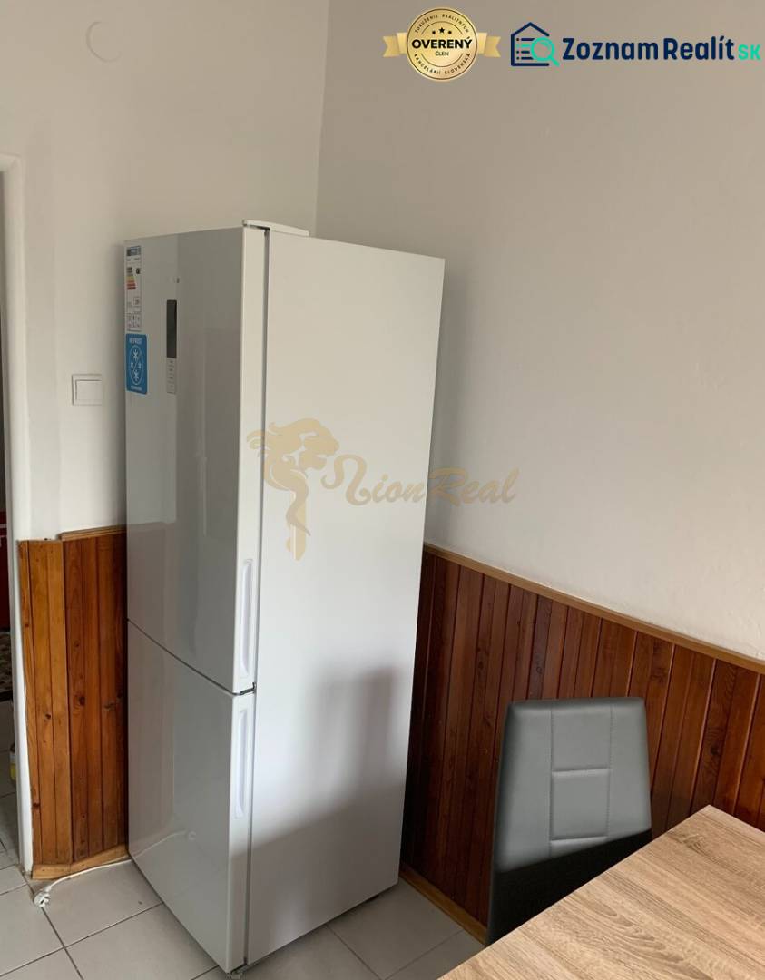 A kitchen in a 2-room apartment with a refrigerator, dark tiles, and a dining area.