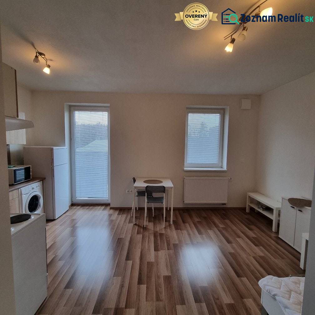 A studio apartment with a wood-patterned floor, a table, and appliances.