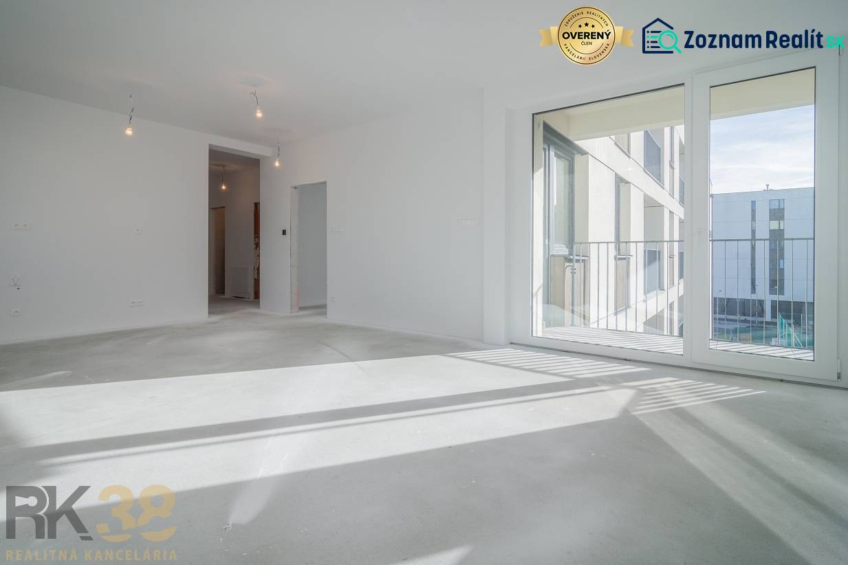 A room in a 3-room apartment with a large window, wooden decor flooring, white walls.