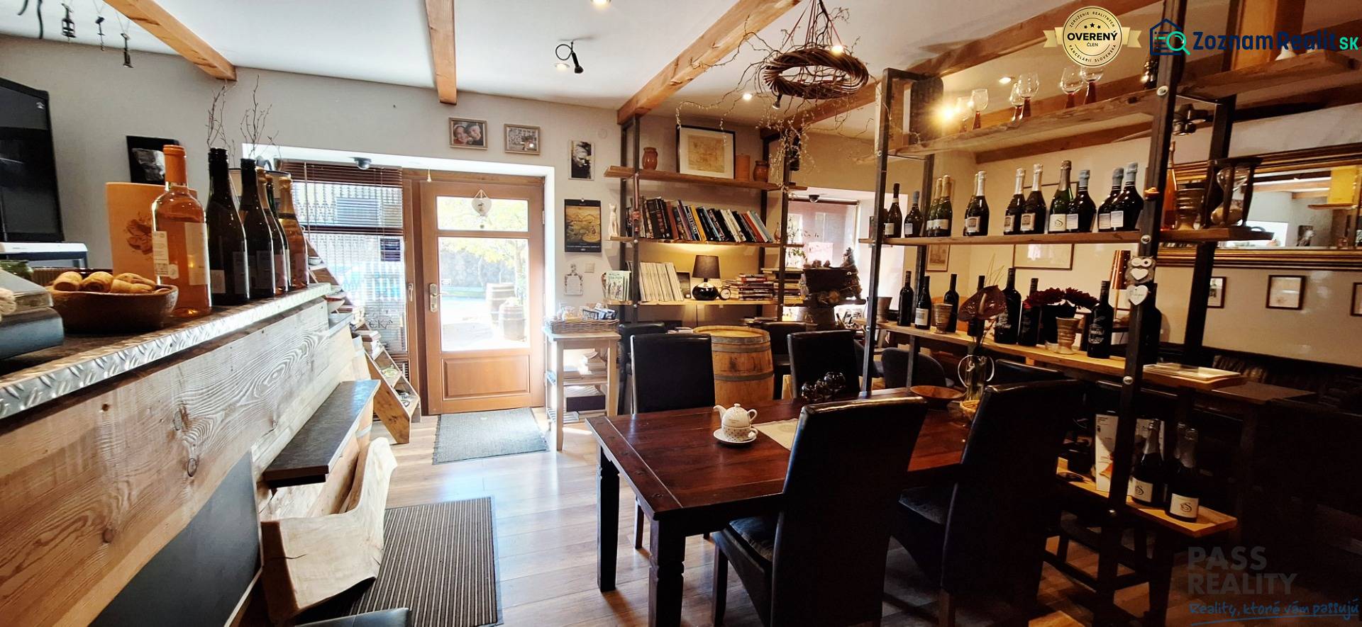Interior of commercial space with a bar, table, and wine shelves, floor with wooden decor.