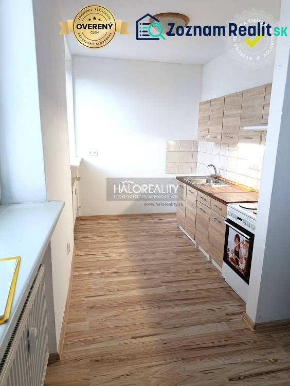 The kitchen of a one-room apartment with a kitchen unit on a floor with a wooden decor.