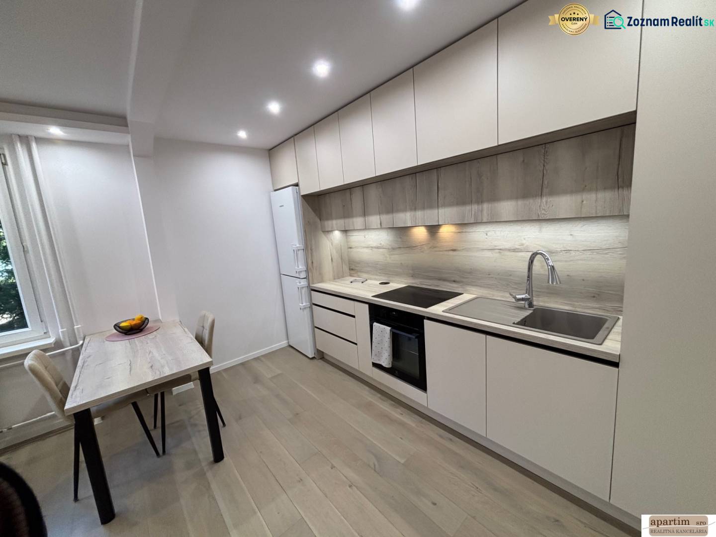 A kitchen in a 2-room apartment with a wooden decor floor, a dining table, and a kitchen unit.