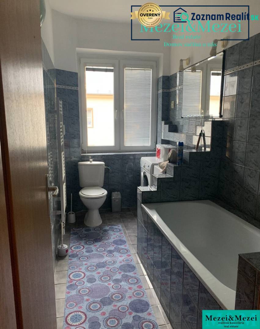 Bathroom in a 2-room apartment with a bathtub, washing machine, and dark tiles.