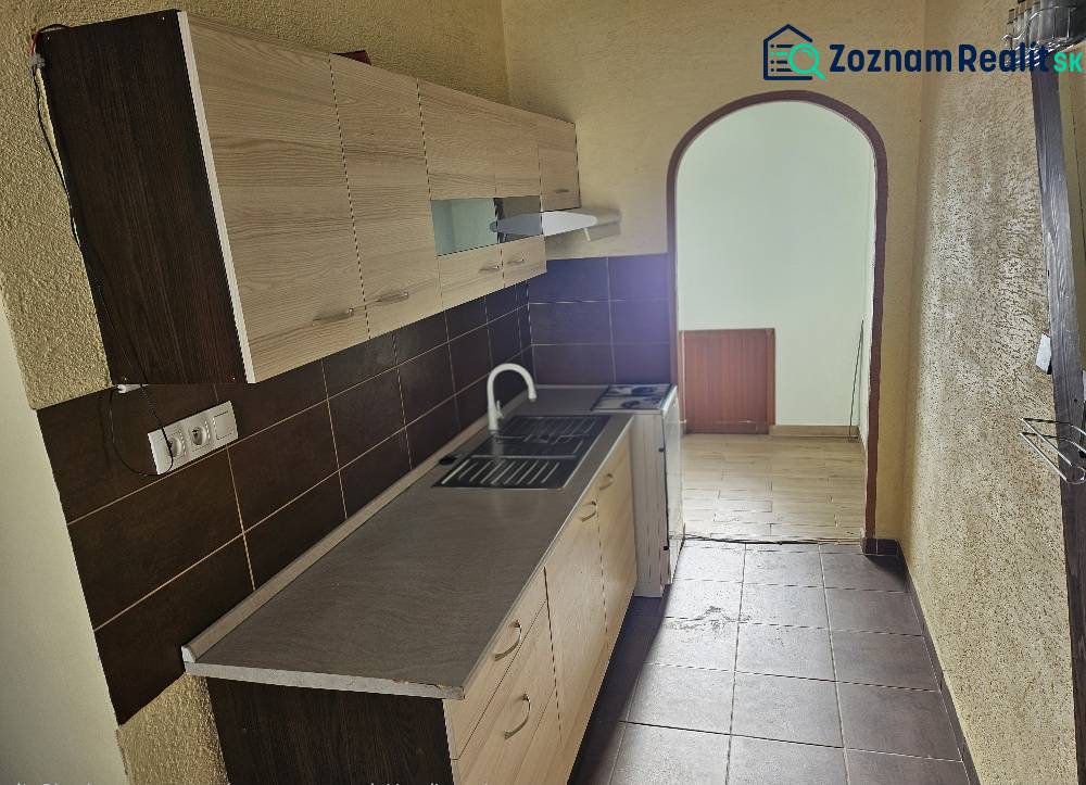 A kitchen in a 2-room apartment with brown tiles and a wooden decor floor.