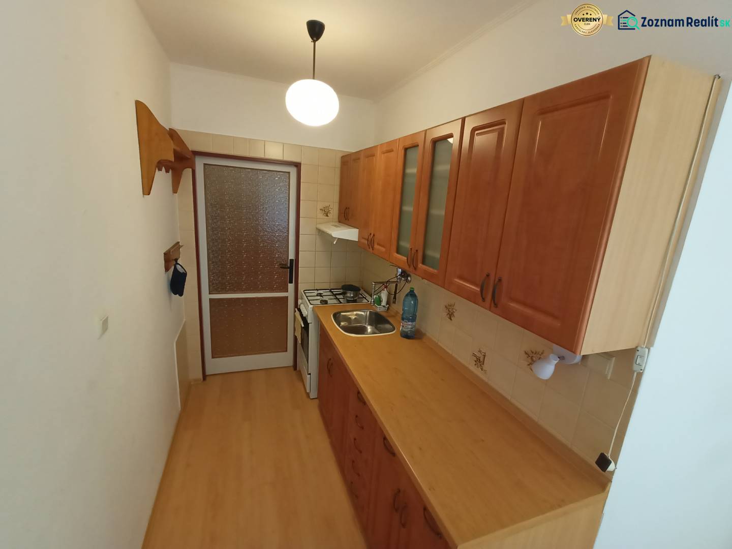 A kitchen with a wood-patterned floor, a kitchen unit, and a gas stove in a two-room apartment.