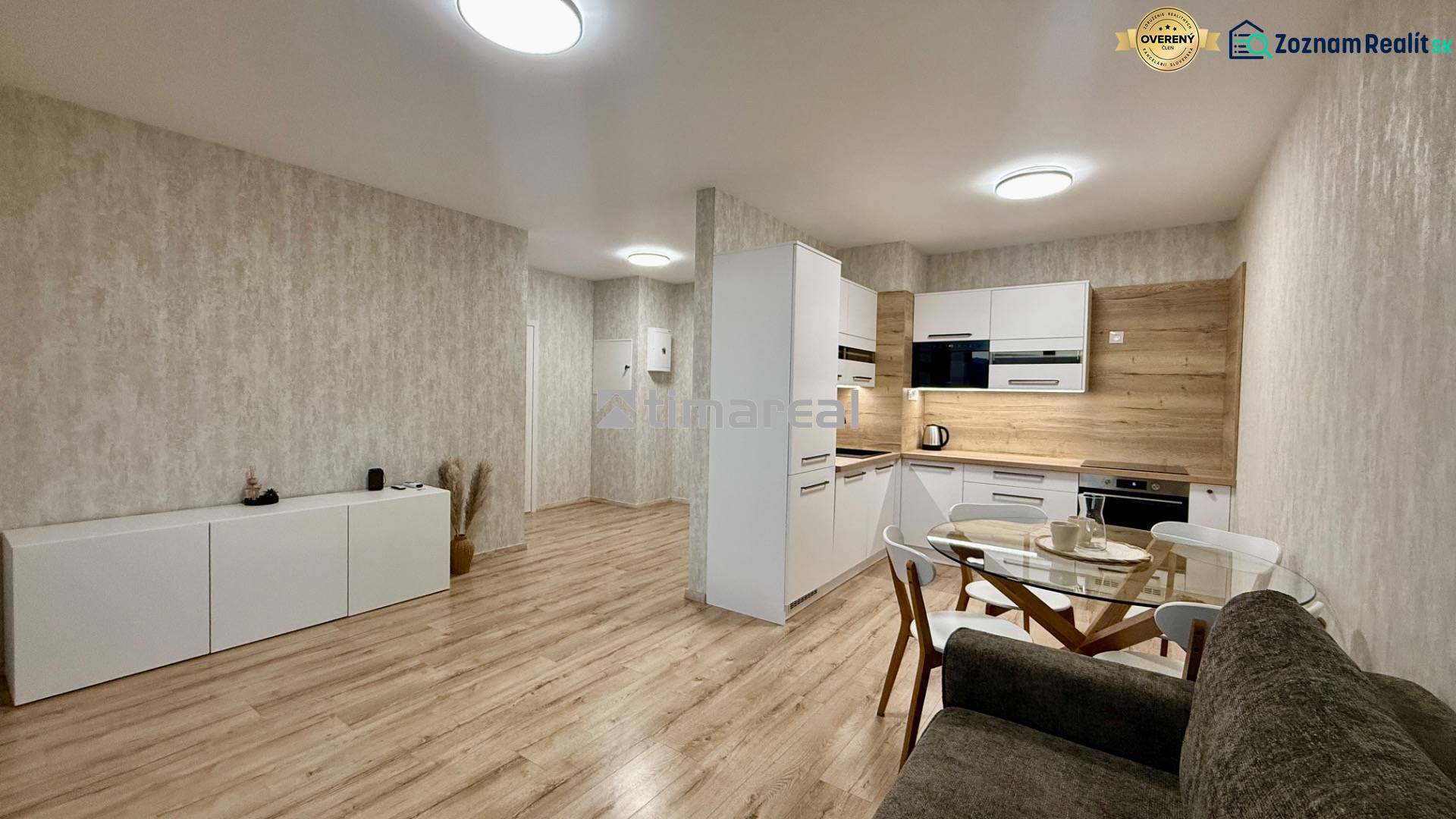 A kitchen in a 2-room apartment with a wooden decor floor and a glass dining table.