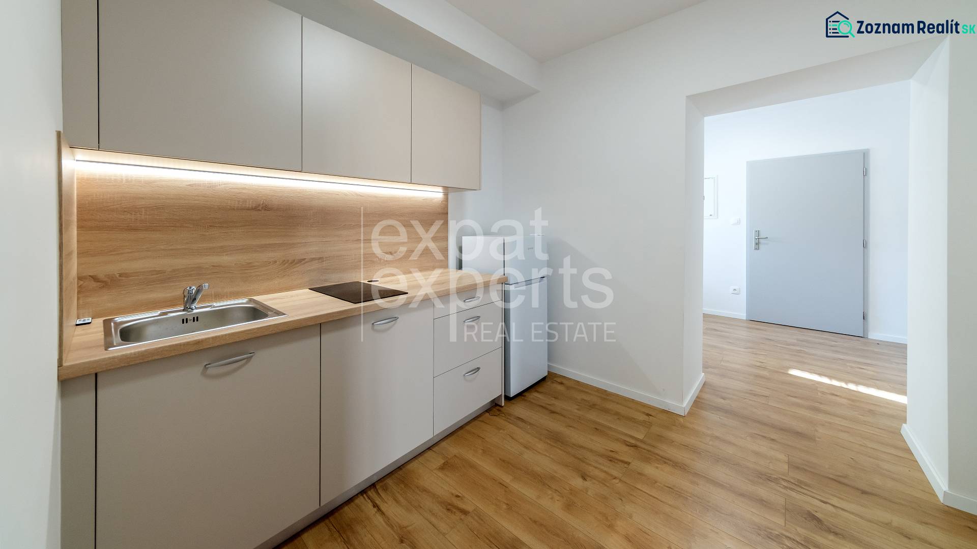 Kitchen unit with wood decor, hob, sink, and entrance to the room in a 2-room apartment.