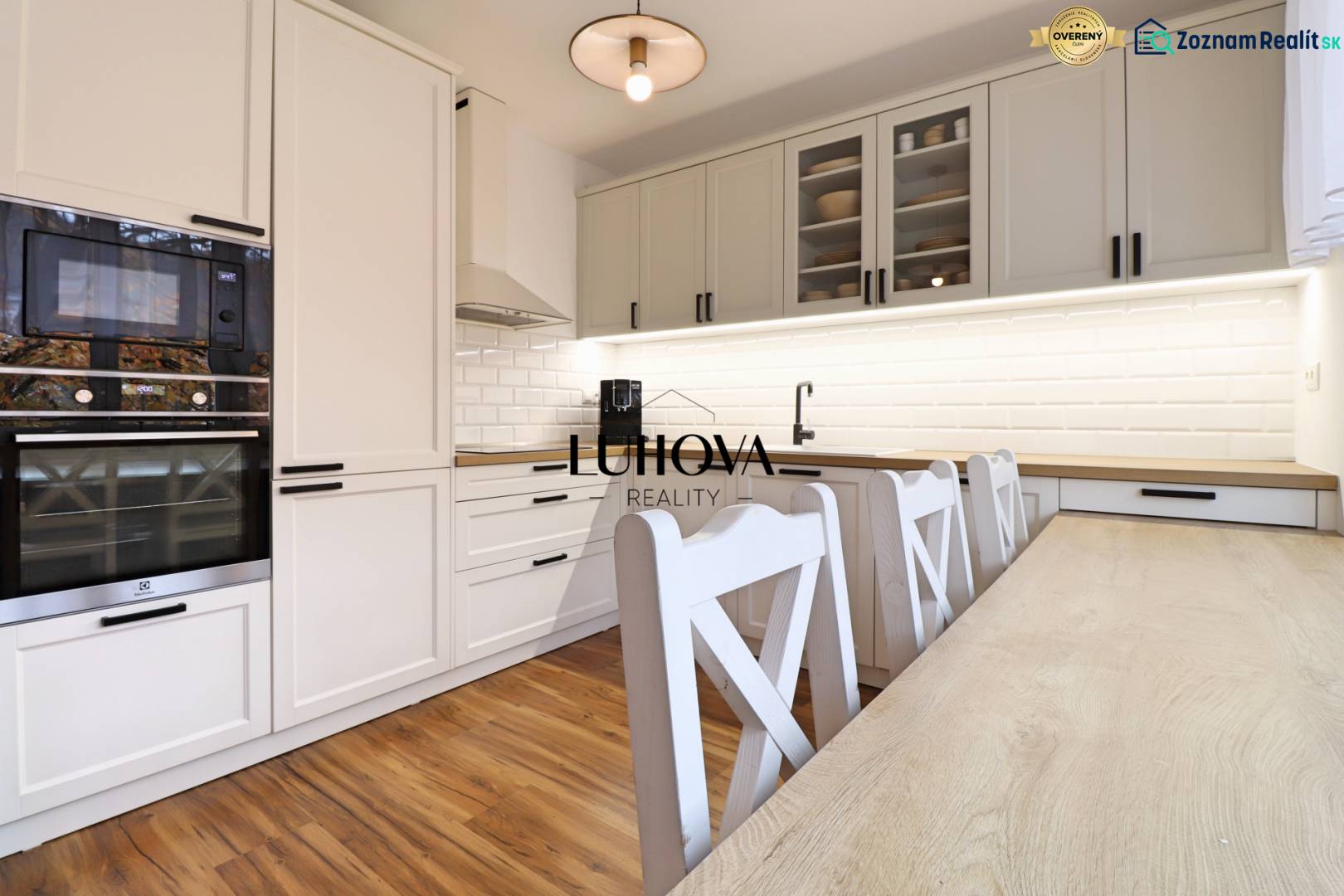 A kitchen in a 3-room apartment with a wooden decor floor and white kitchen cabinets.
