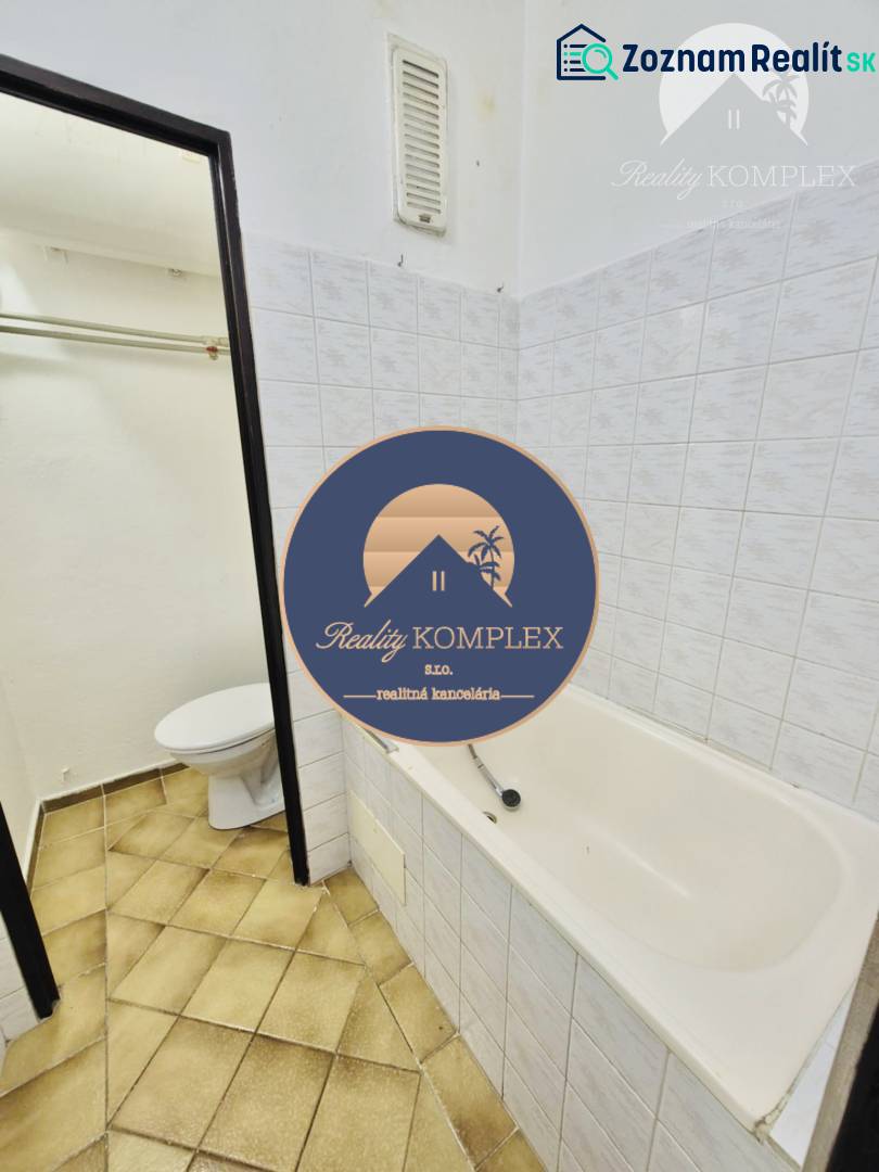 Bathroom in a studio apartment with a bathtub and toilet, tiles in brown shades.