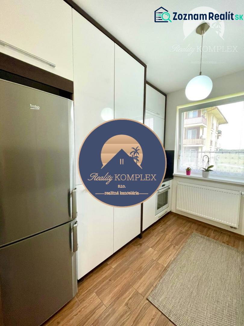 A kitchen in a 2-room apartment with white cabinets, a refrigerator, and a wooden decor floor.