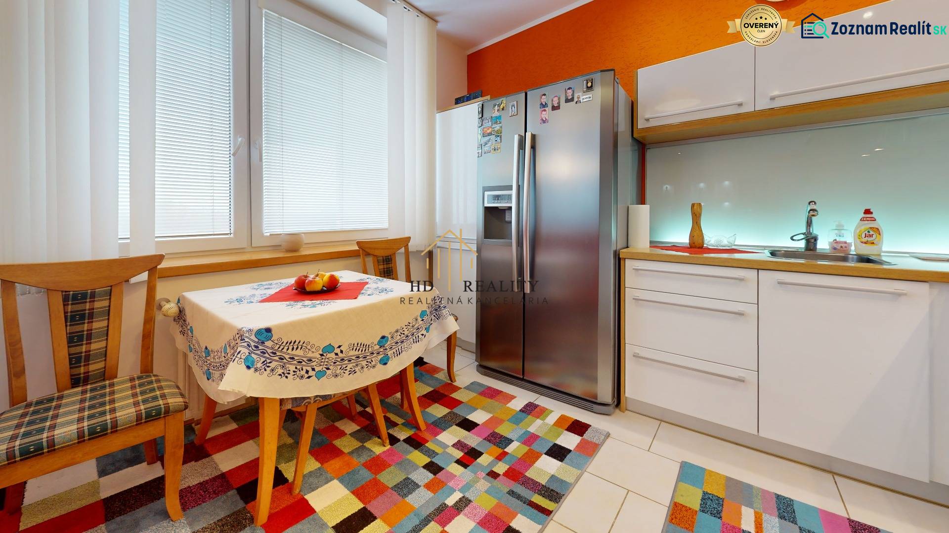 A kitchen in a 2-room apartment with bright colors, a dining table, and a large refrigerator.