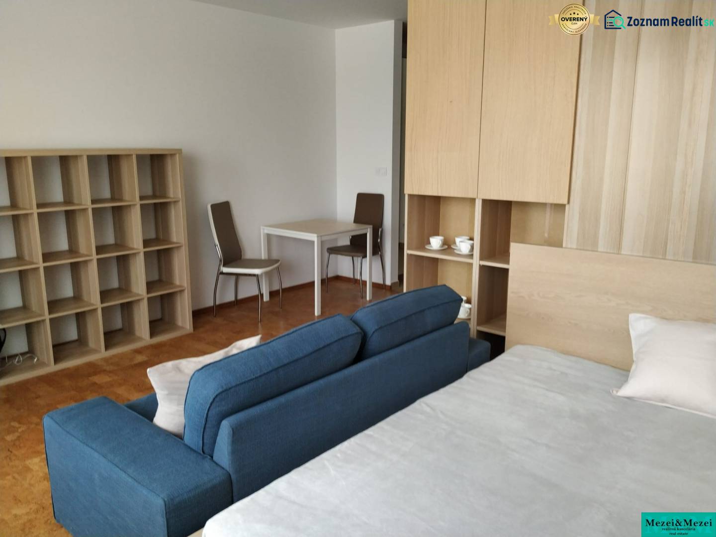 Bright living area with a blue sofa, desk, and shelves in a studio apartment.