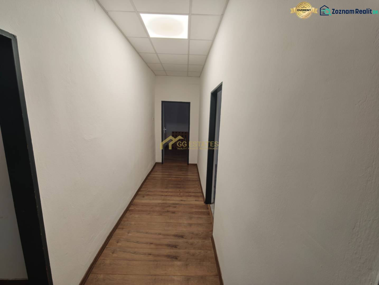 A hallway in an office with white walls and a wooden decor floor.