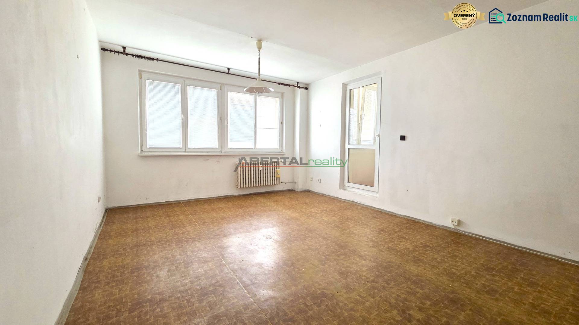 A room with a wooden floor, white walls, and a large window.