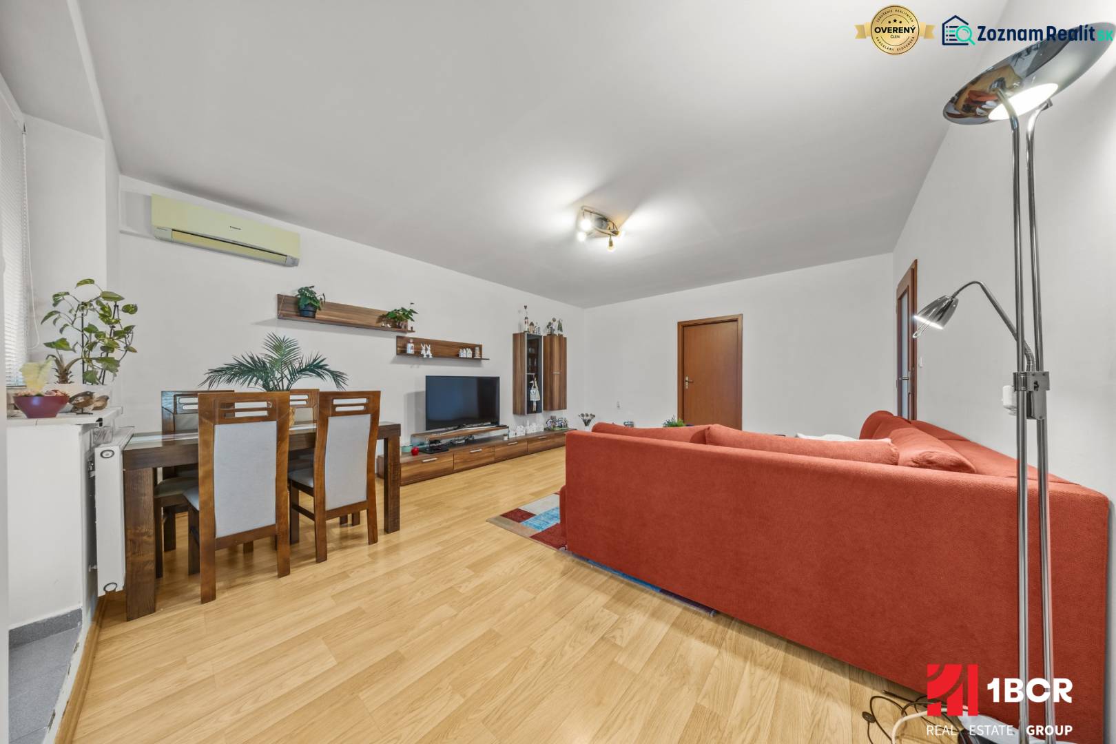 Living room in a two-room apartment with a wooden decor floor and a red sofa.