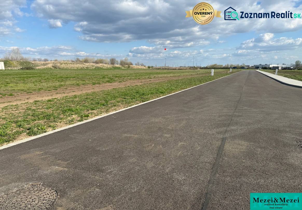 An asphalt road leading between green commercial properties in Trnava under a cloudy sky.