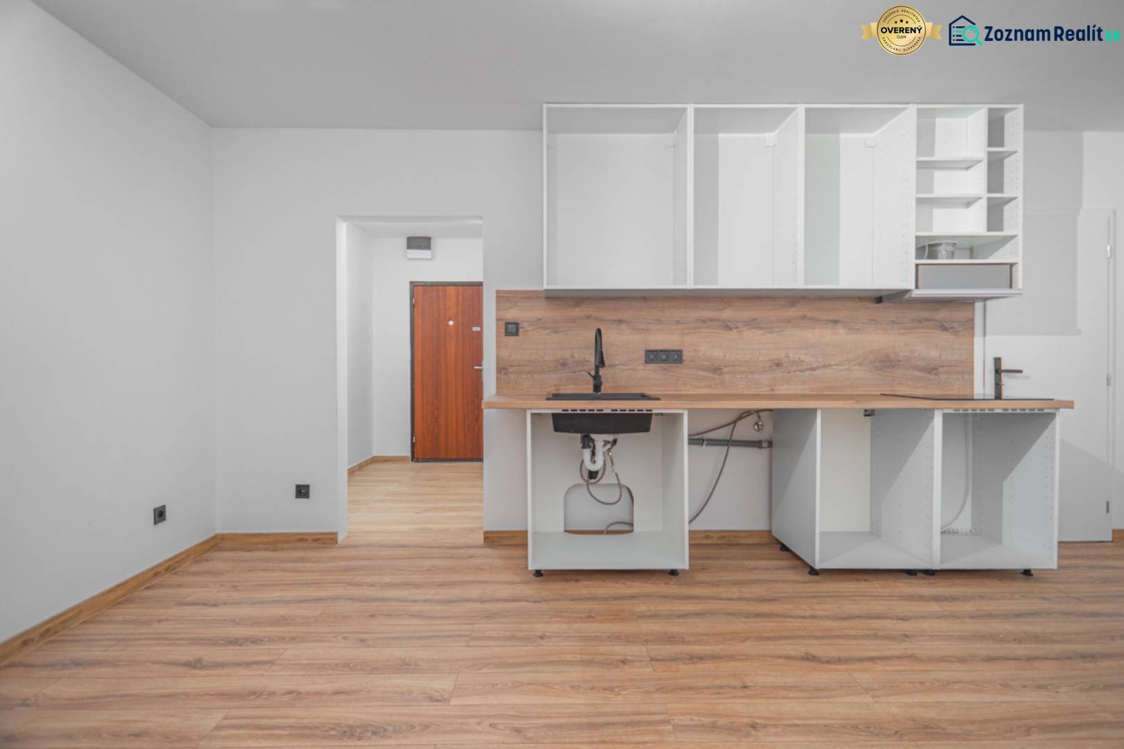 An empty kitchen unit with wood-decor flooring in a studio apartment.