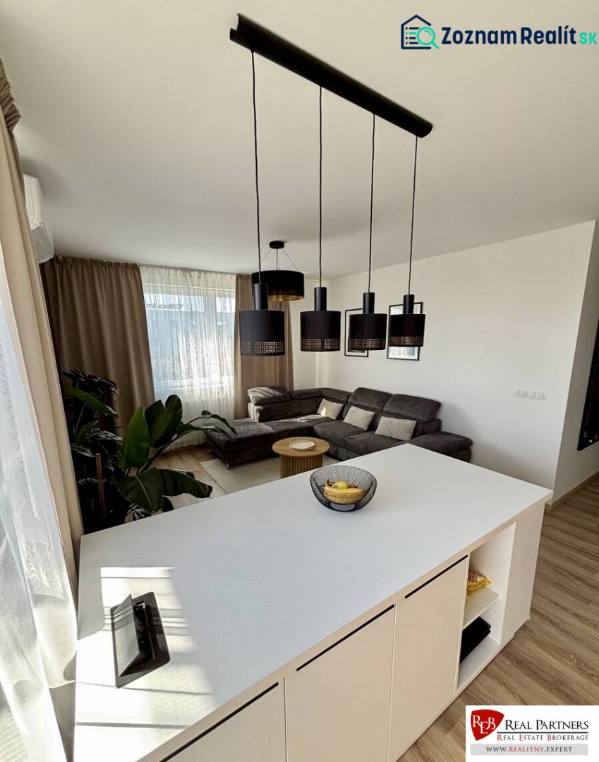 A bright open kitchen with a counter, sofa, and wooden decor flooring in a three-room apartment.
