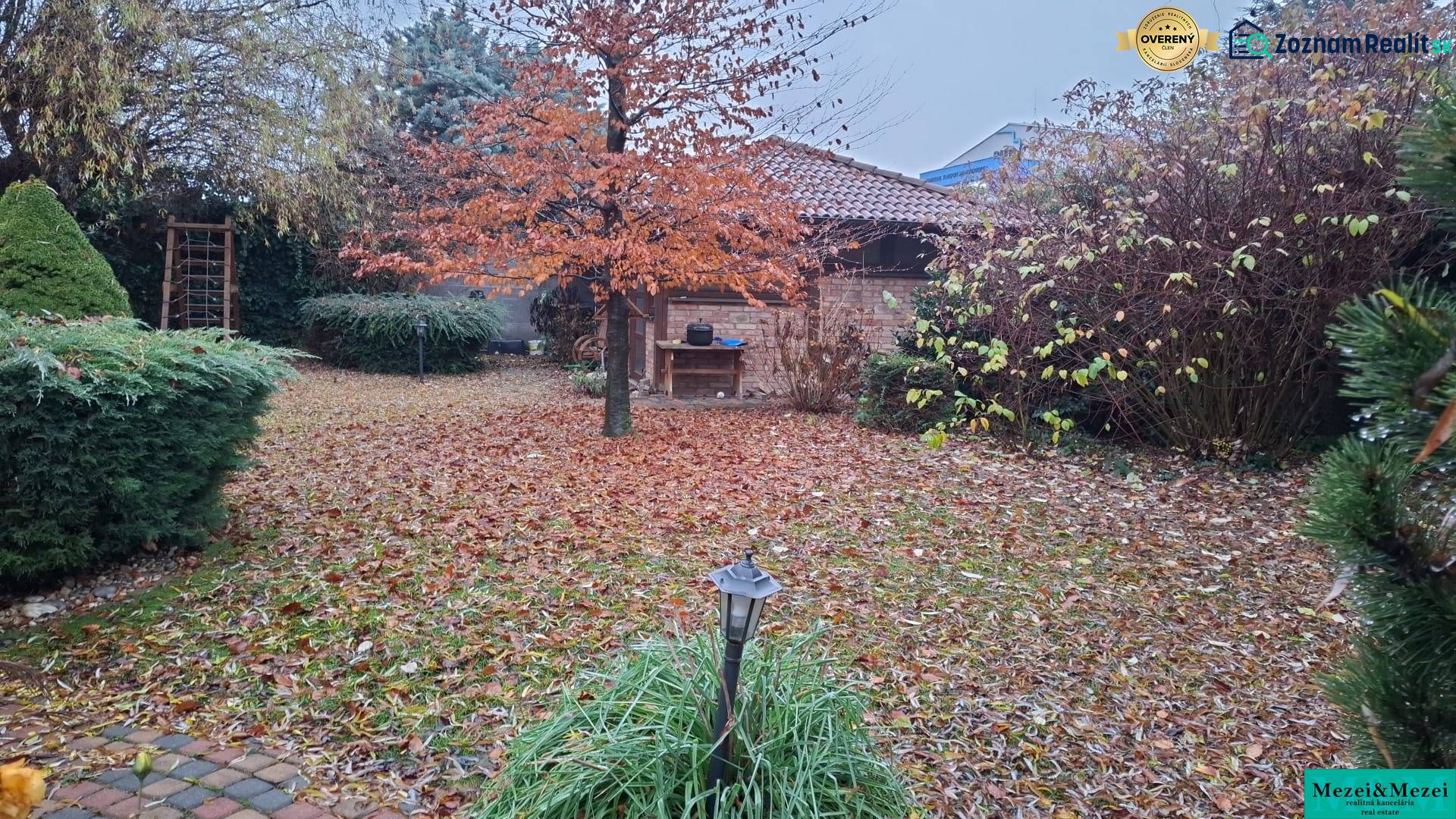 The garden of a family house in Bohdanovce nad Trnavou with autumn leaves and a small structure.