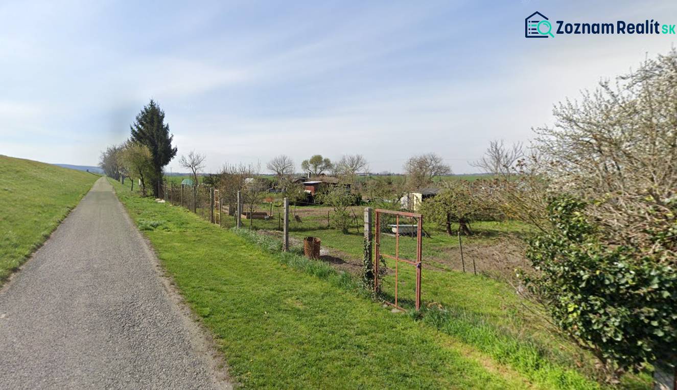 Recreational plots in Drahovece with a road, fence, trees, and maintained lawn along the access road.
