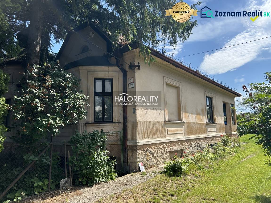 A family house with wooden windows, stone foundations, surrounded by bushes and a blooming garden.